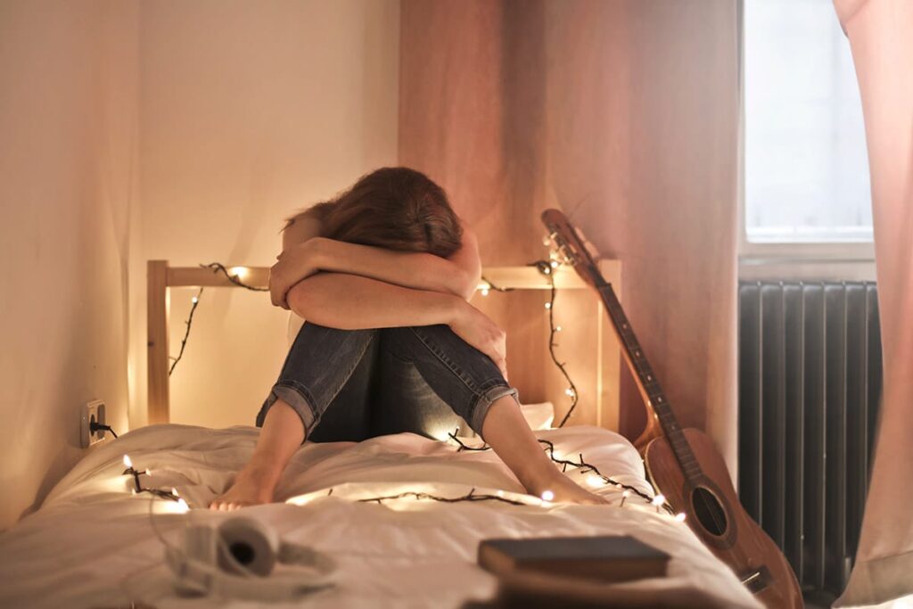 teenager sitting on their bed with their head wrapped in their arms as in indication of identifying a mental health crisis in teens