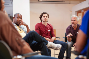 group of young people seated in a circle as part of a group therapy session led by a mental health professional