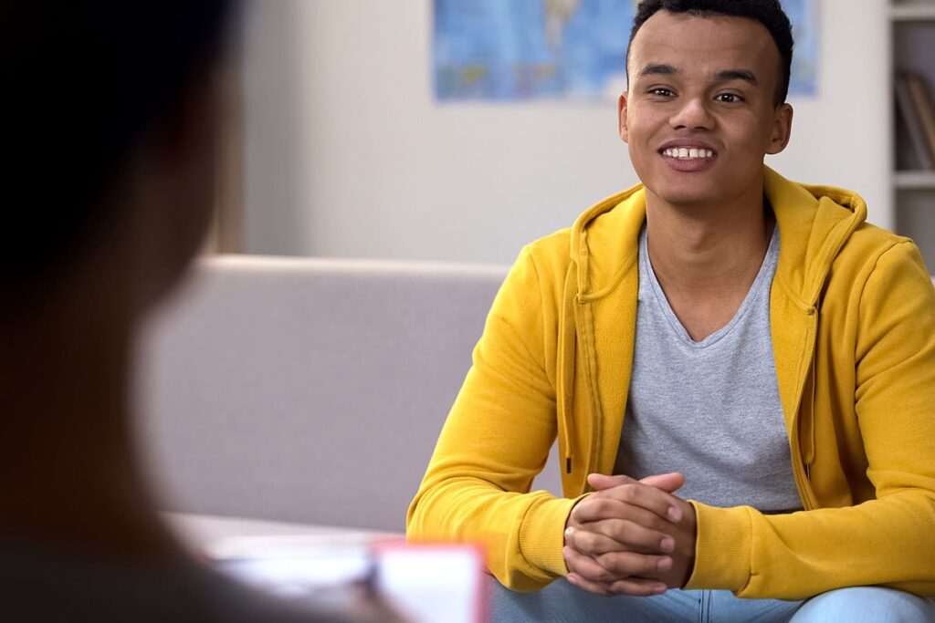 teenage boy smiling and meeting with therapist as he receives the benefits of trauma therapy