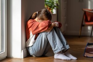 teenage girl seated on floor leaning against the wall with her head in her hands in critical need of a depression treatment program for teens and adolescents