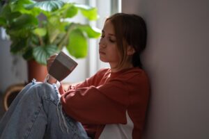 teenage girl leaning against the wall by her window on a sunny day and enjoying the 5 benefits of grief and loss therapy for teens