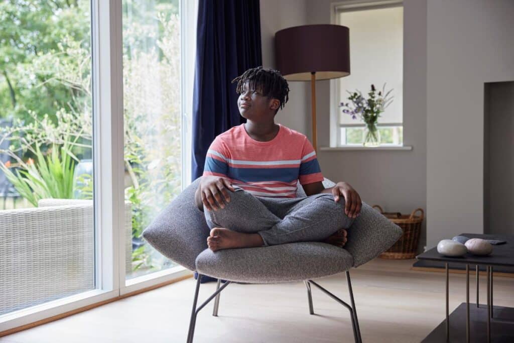 adolescent seated quietly off to themselves in a comfortable chair as one of 5 tips to calm social anxiety in teens.