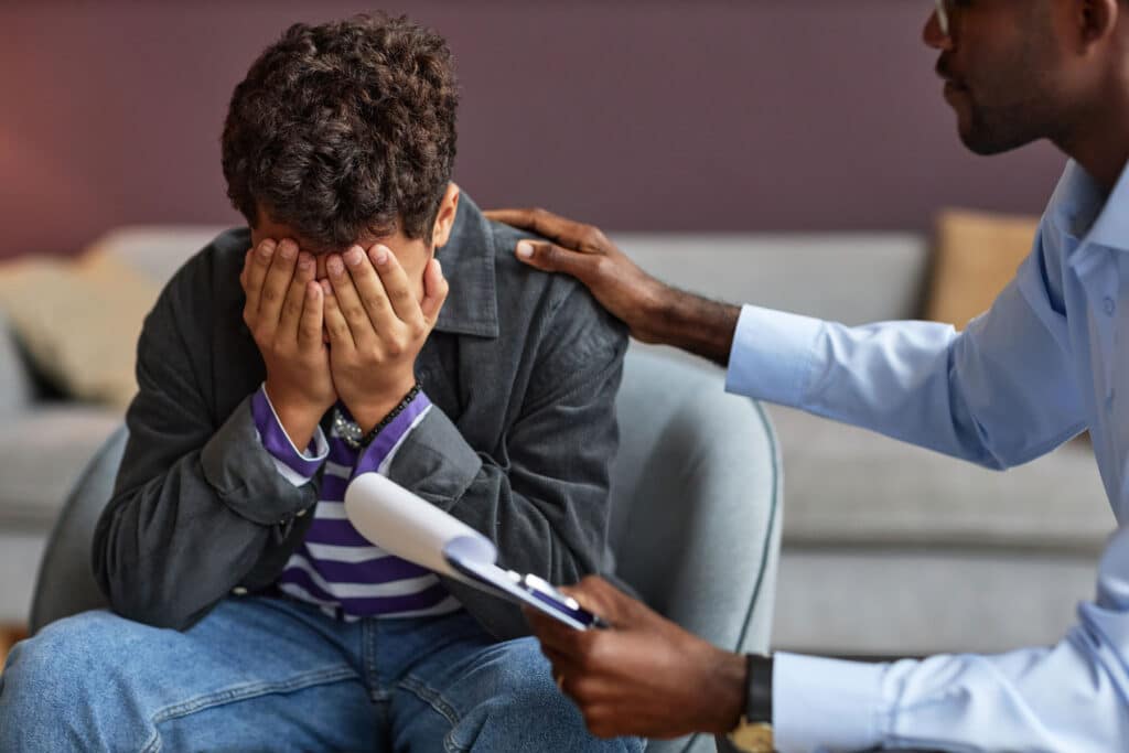distraught teenage boy being consoled by a behavioral health specialist who is helping him to find a teen crisis intervention program in Omaha, NE.