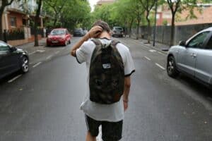 teen boy walking away from camera wearing white shirt and camo backpack